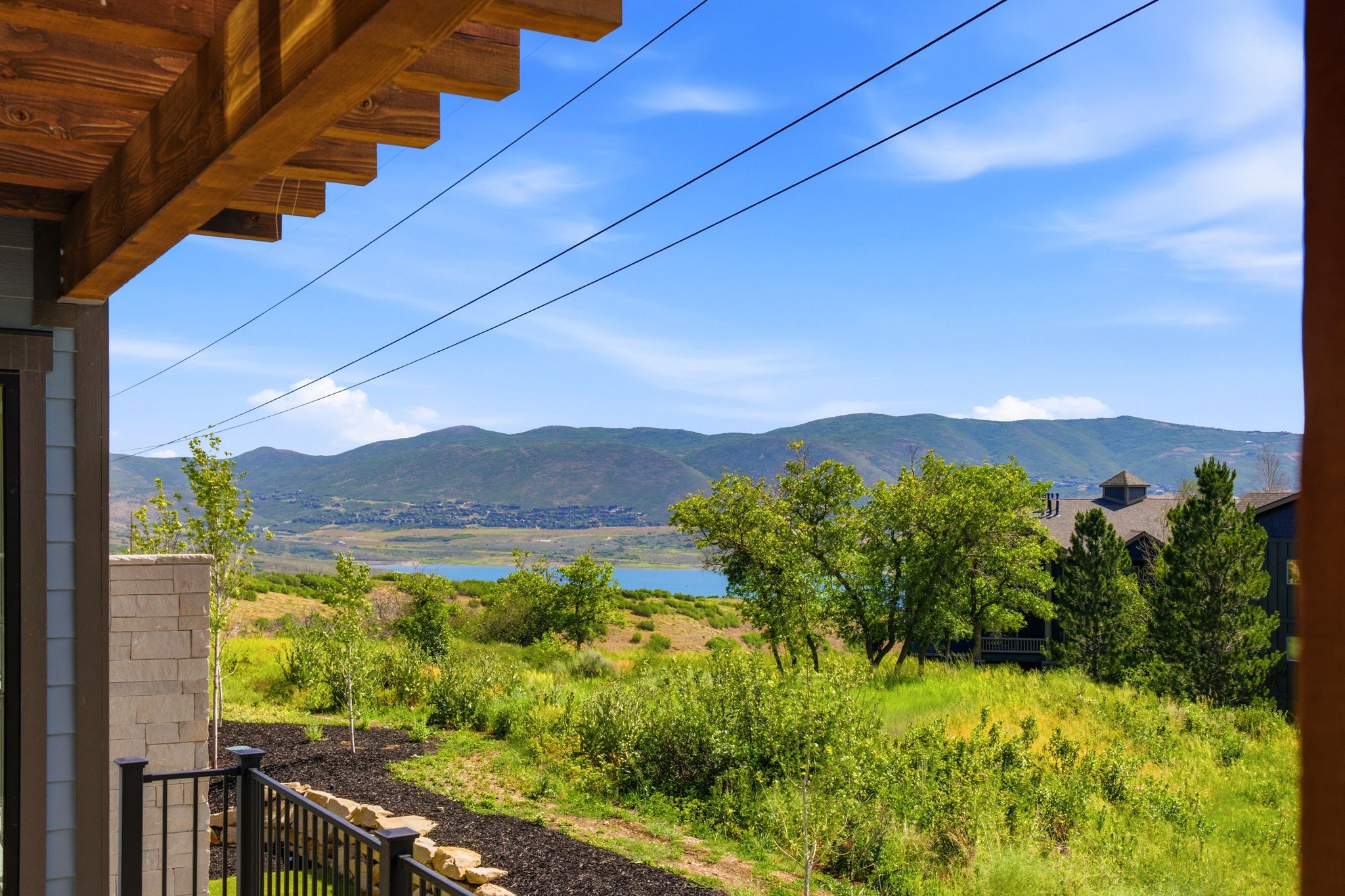 Outdoor living space featuring a wooden beam overhang, black metal railing, and a stone pillar