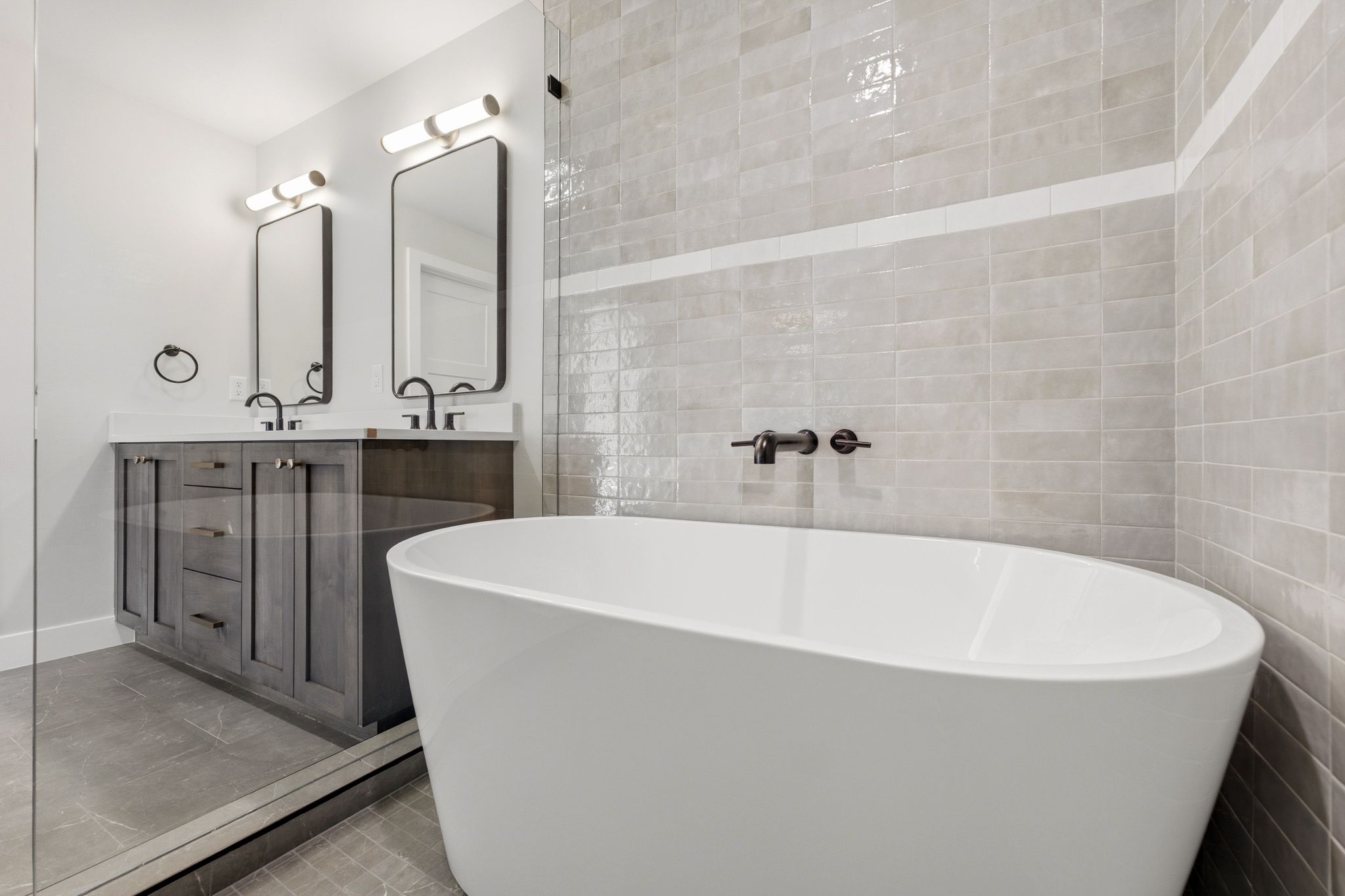 Freestanding soaking tub with wall-mounted matte black faucet, surrounded by large format and subway-style tile