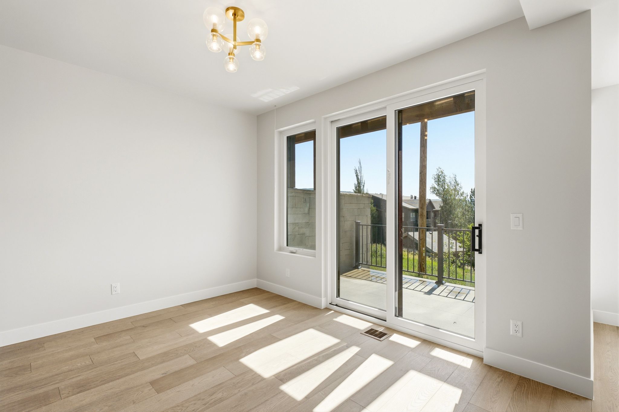 Light-filled room featuring wood-finish flooring, white baseboards, and a modern gold-tone chandelier
