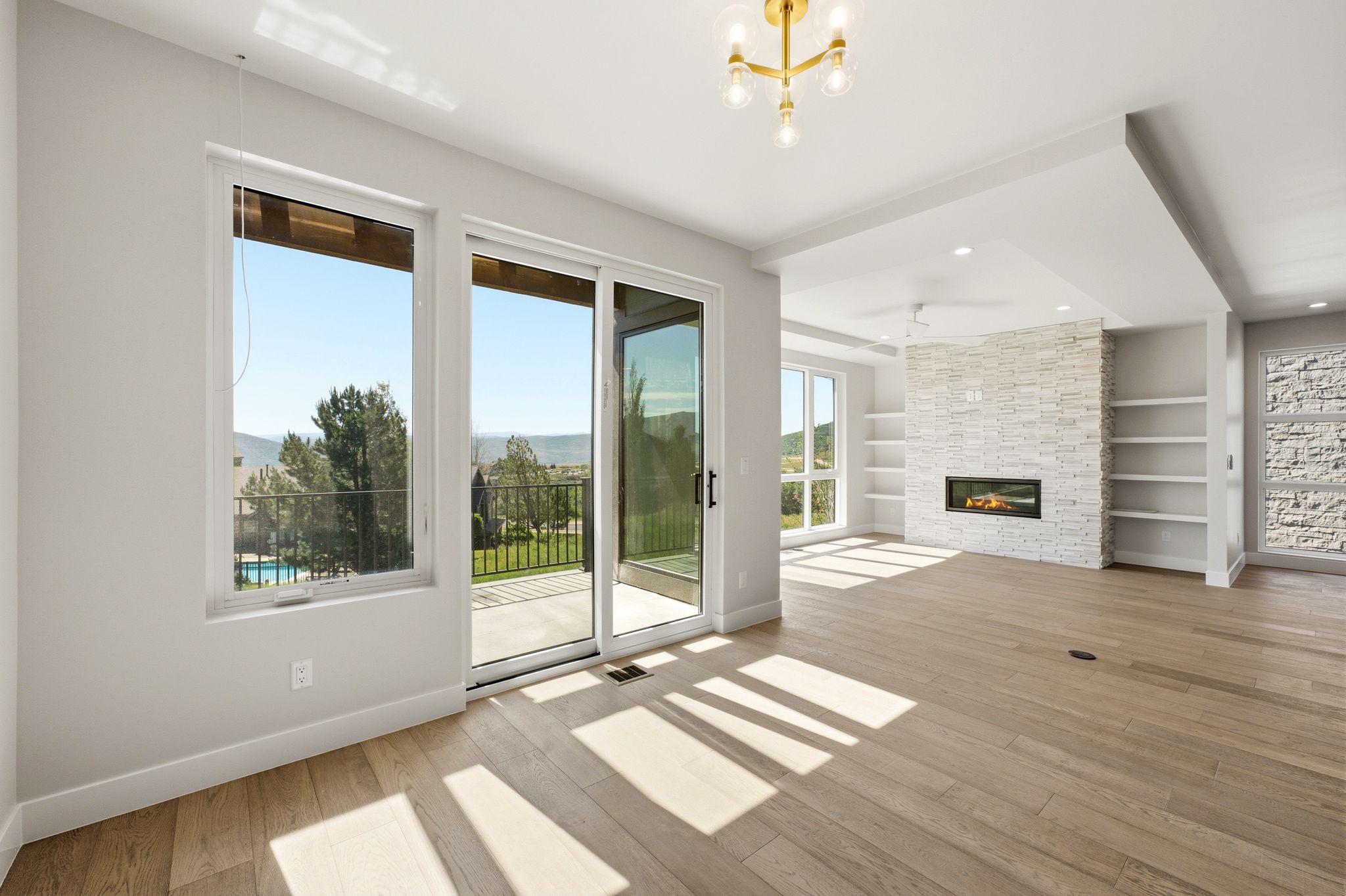 Spacious living area featuring wood-finish flooring, an integrated linear fireplace with a stacked stone surround, and built-in shelving