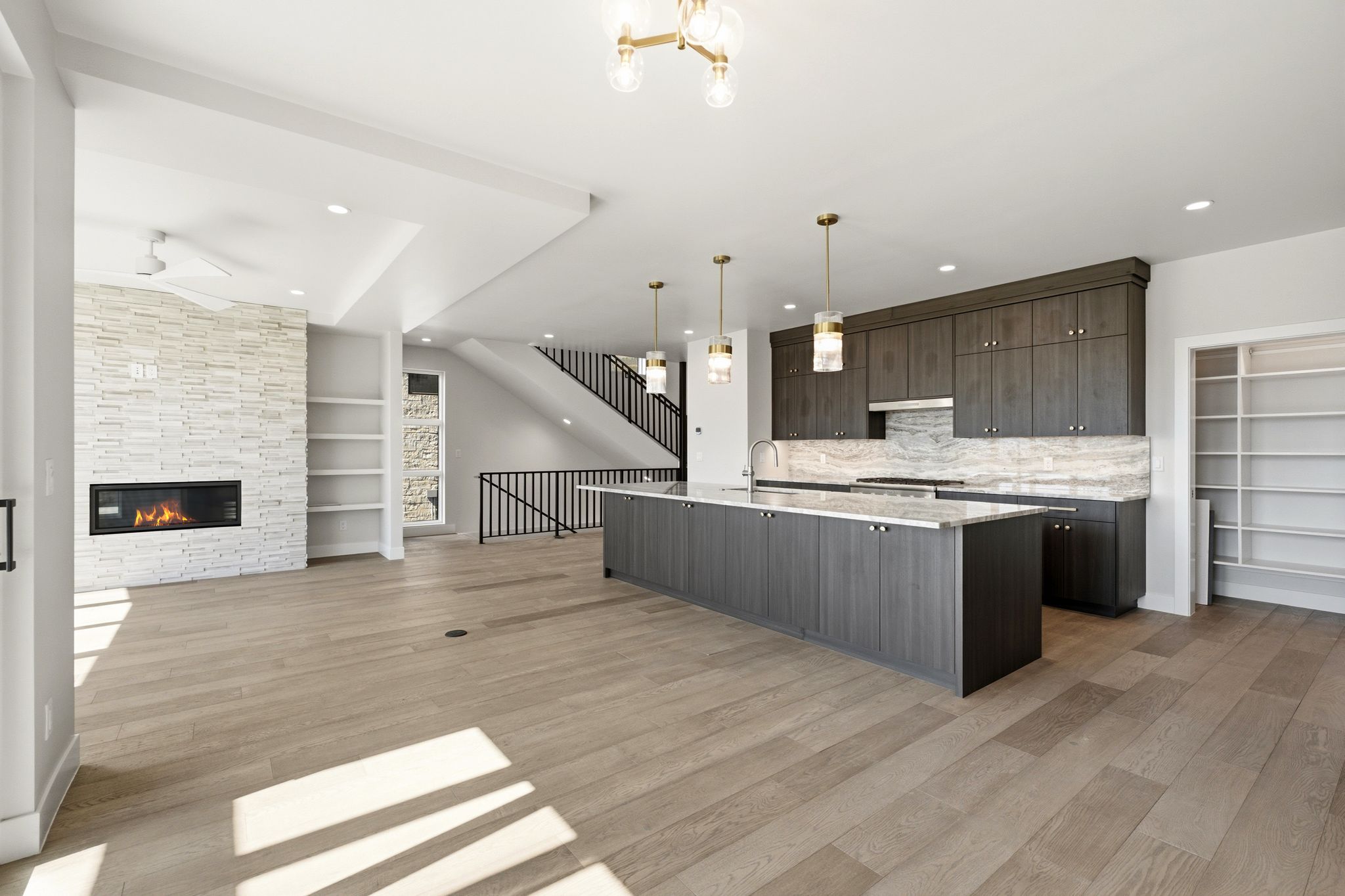 Open-concept living space featuring wood-finish flooring, a contemporary fireplace with a stacked stone surround, and built-in shelving