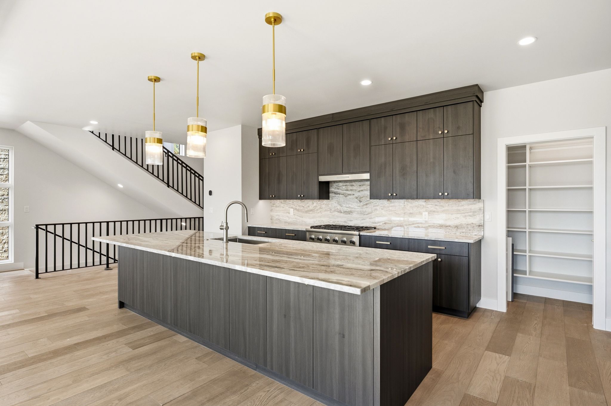 Modern kitchen featuring a large island with an undermount sink, brass pendant lighting, stainless steel range, and a built-in pantry