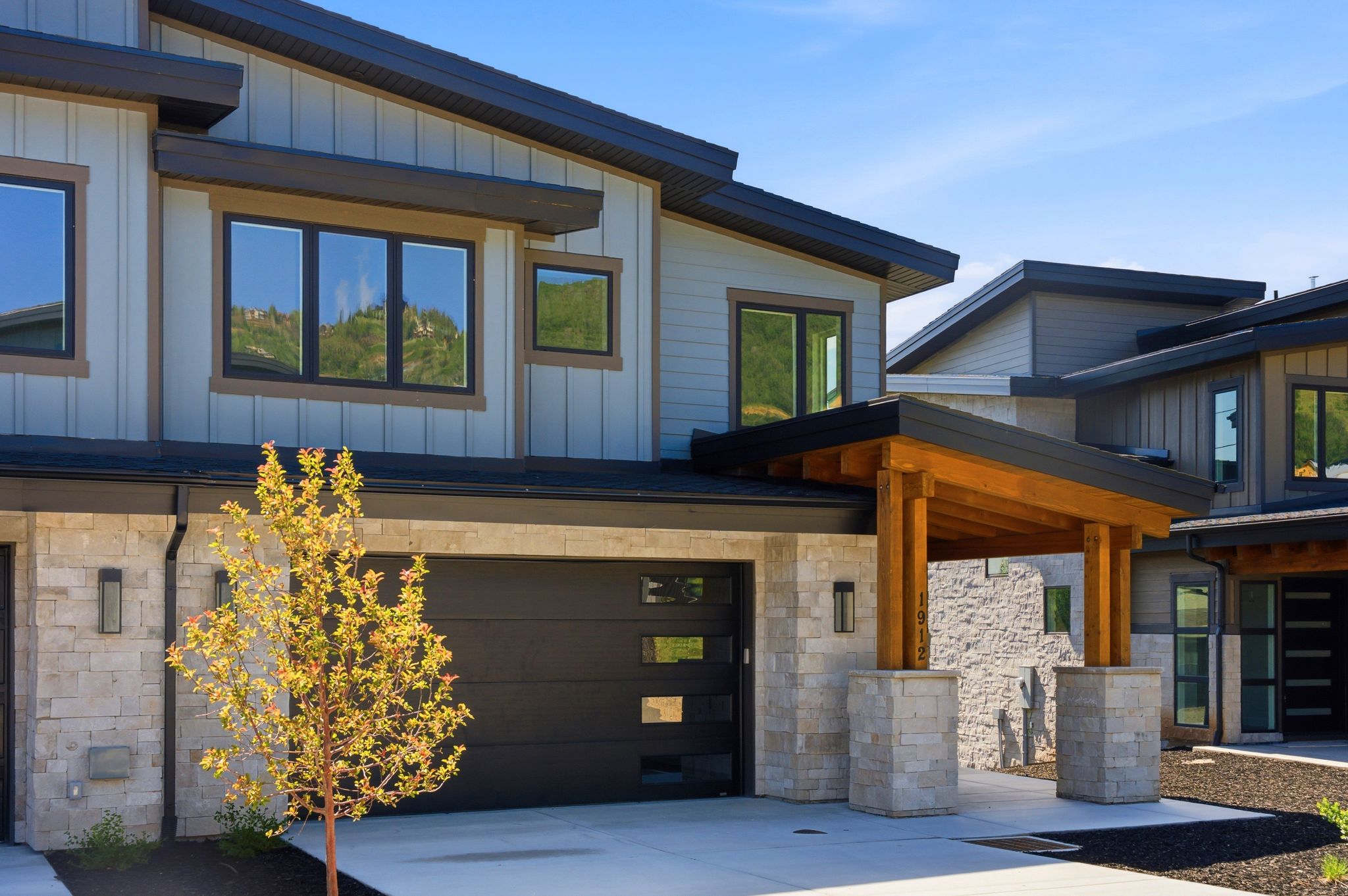 Contemporary facade featuring light-toned siding, dark trim, and stone accents
