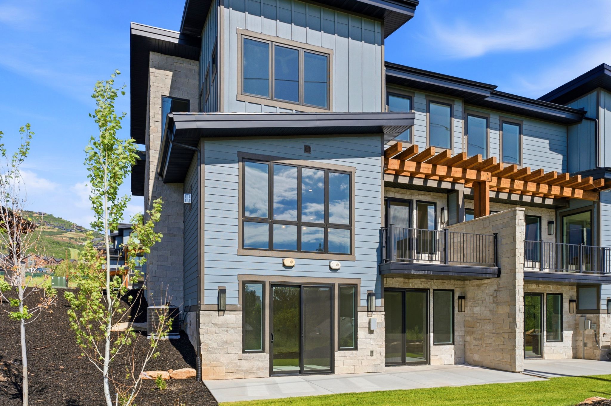 Modern multi-level exterior with board-and-batten and horizontal siding accents, stone veneer foundation, and multiple balconies featuring a wooden pergola and metal railings