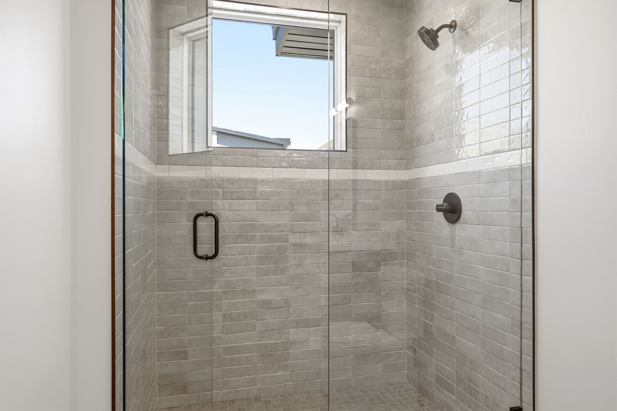Glass-enclosed shower with gray subway tile walls, a horizontal accent tile band, and a window for natural illumination