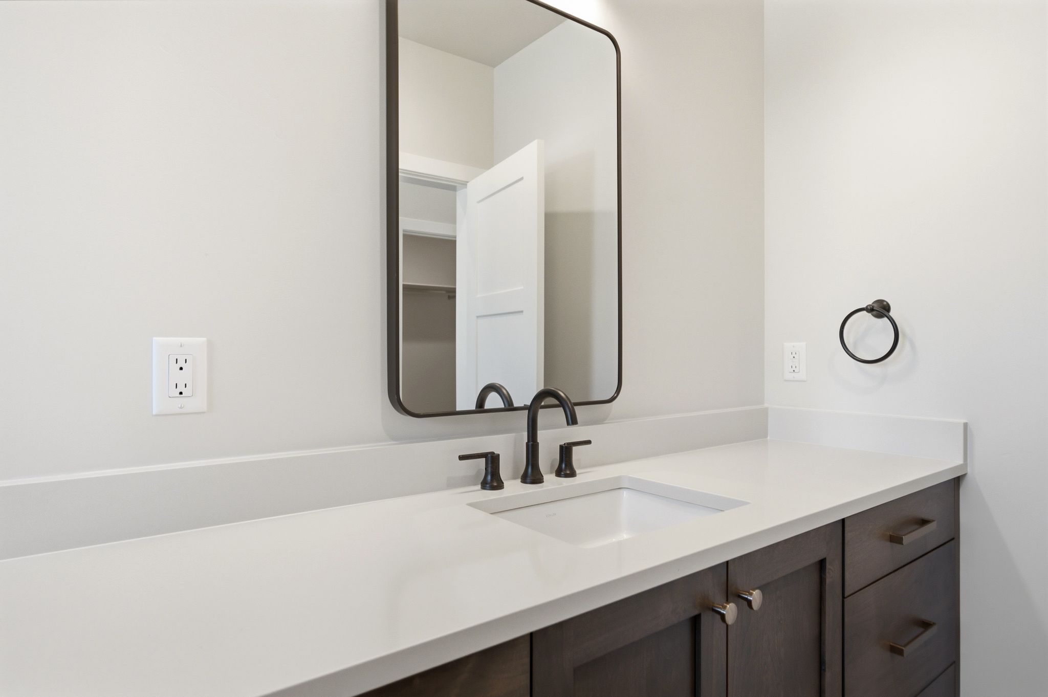Bathroom vanity featuring a rectangular undermount sink, a light-toned countertop, and dark wood-finish cabinetry with silver-toned hardware