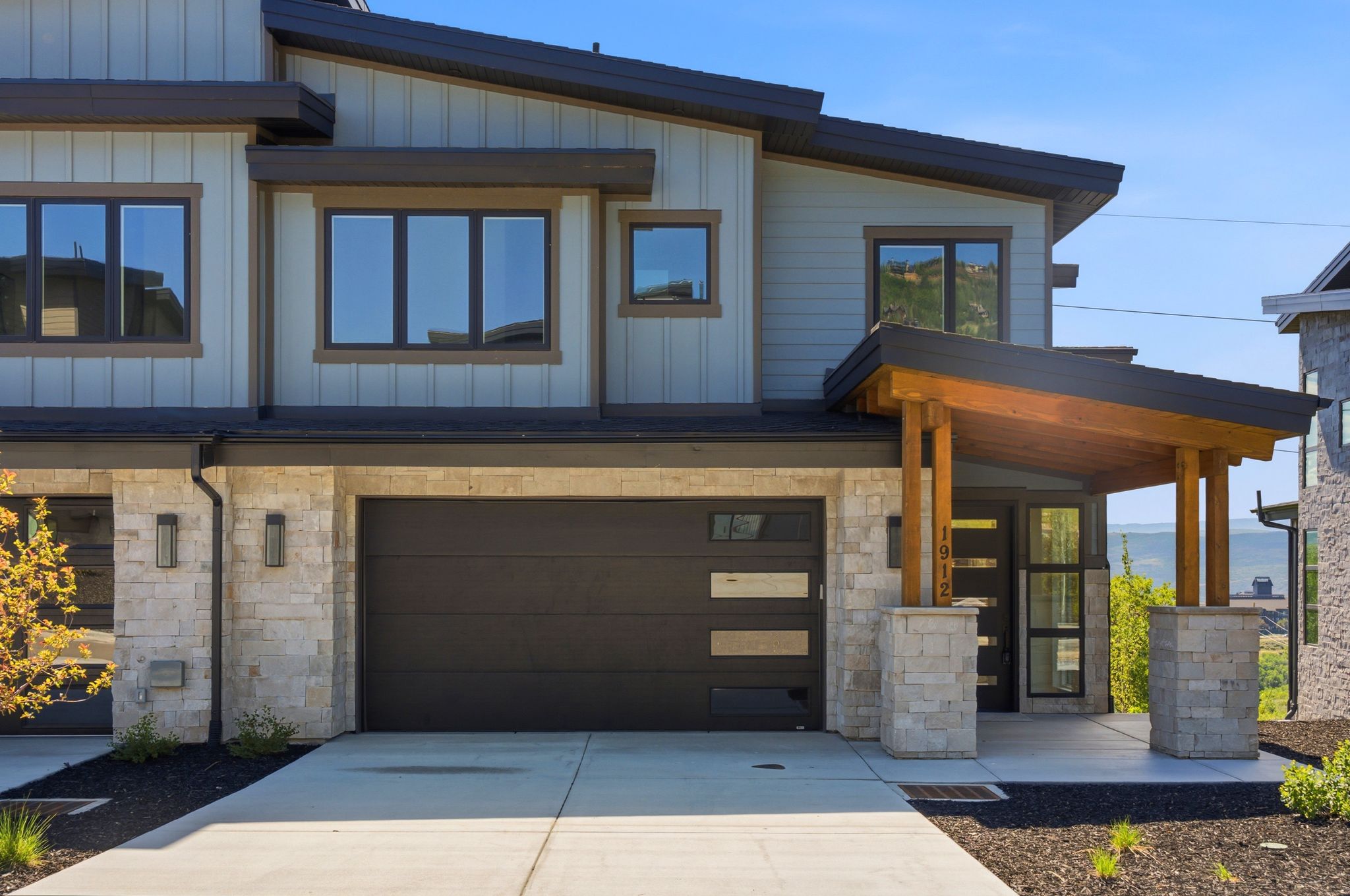 Modern architectural exterior featuring a prominent two-car garage, stone accents, wood-finish columns, and a covered entry