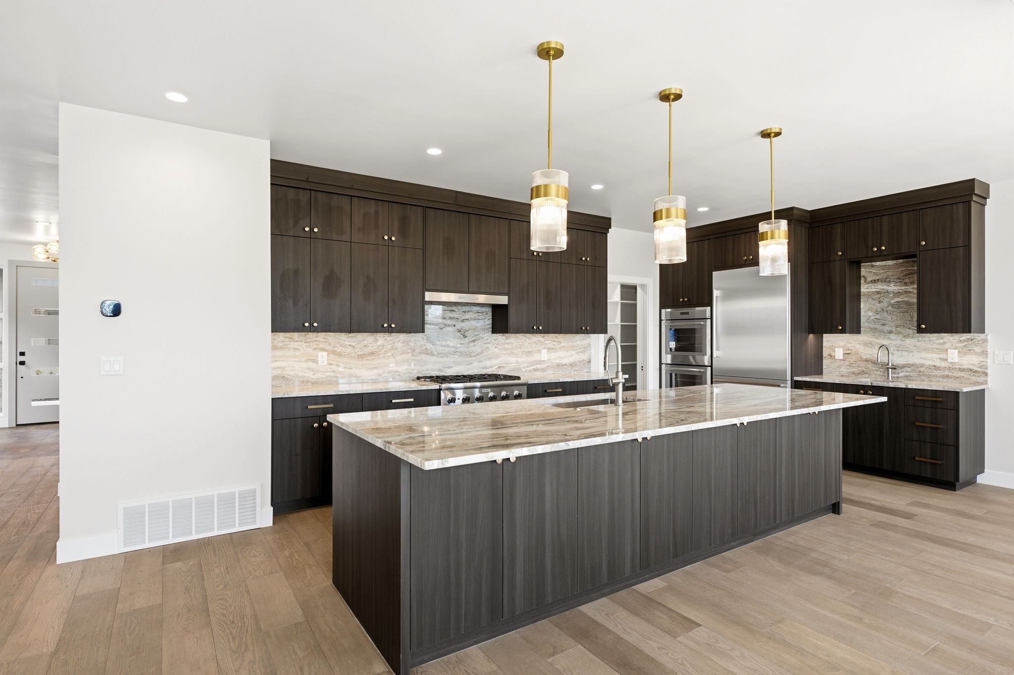 Spacious kitchen featuring an oversized island with countertop seating, dark wood-finish cabinetry, stainless steel appliances, and elegant pendant lighting