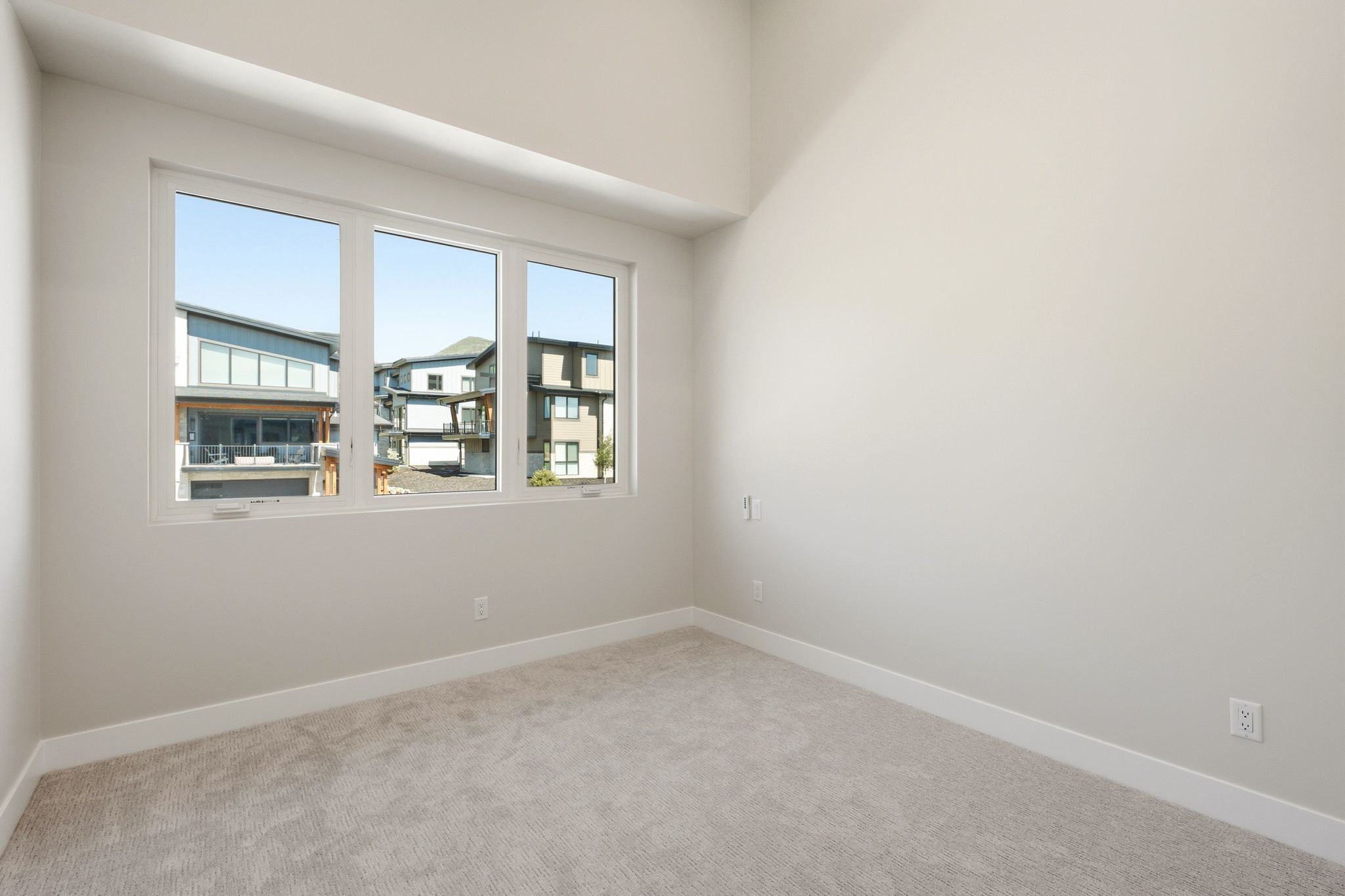 Light-filled room featuring a tripartite window, light-toned carpeting, white baseboards, and neutral wall tones
