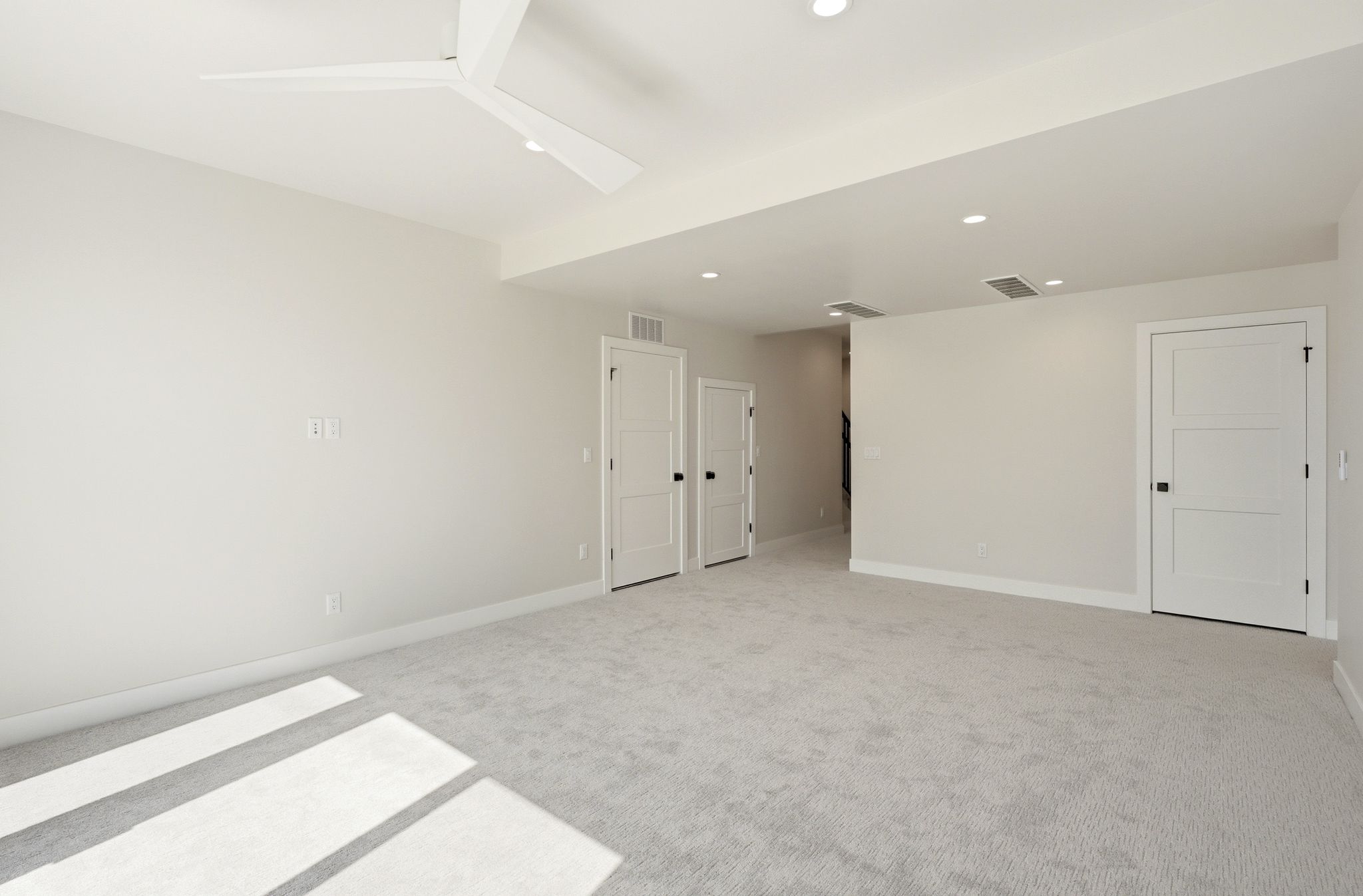 Spacious room featuring light gray carpeting, neutral wall finishes, and a contemporary ceiling fan