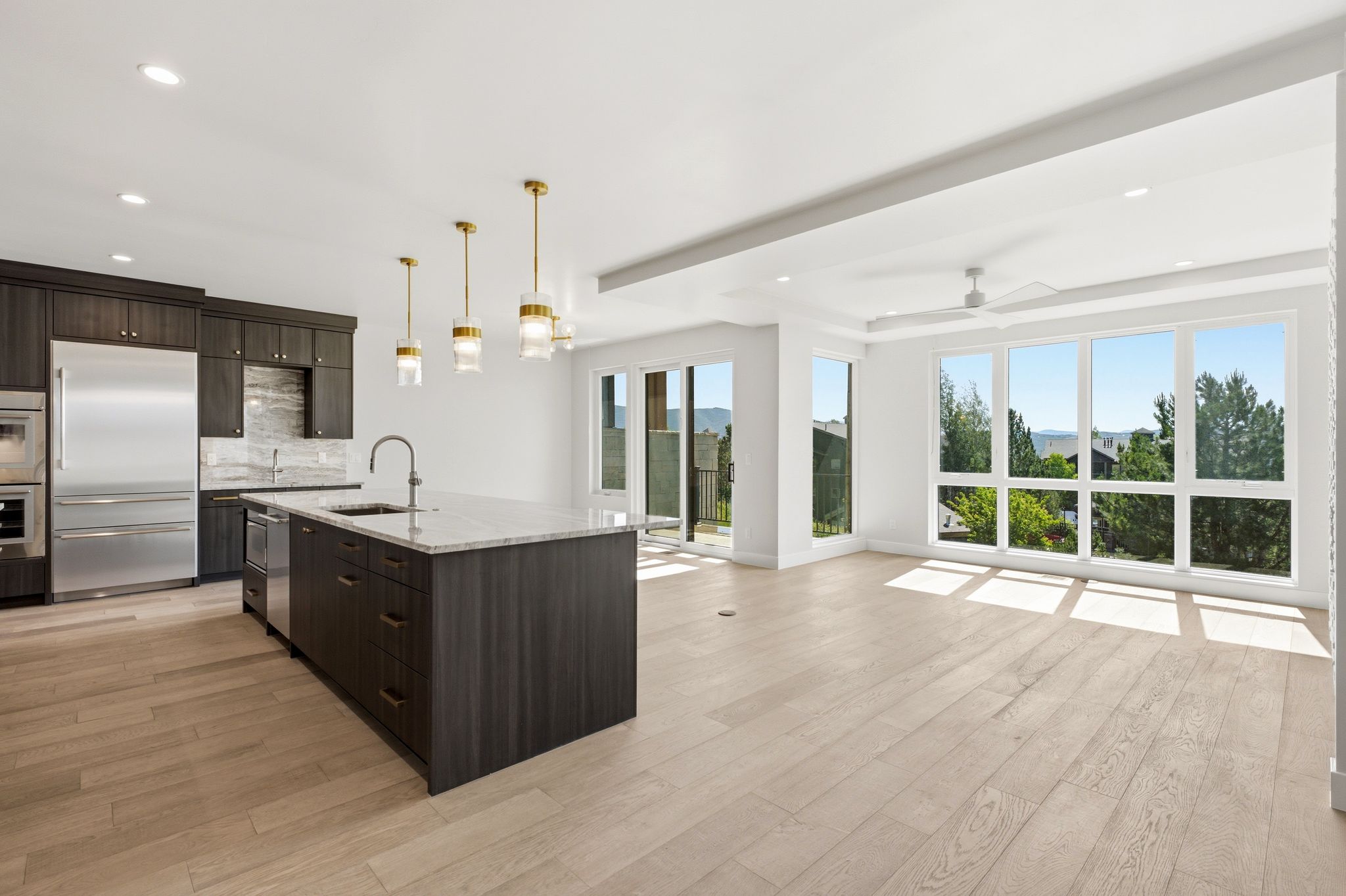 Open-concept interior featuring light wood-finish flooring, a kitchen island with a single-basin sink, stainless steel appliances, and dark wood cabinetry