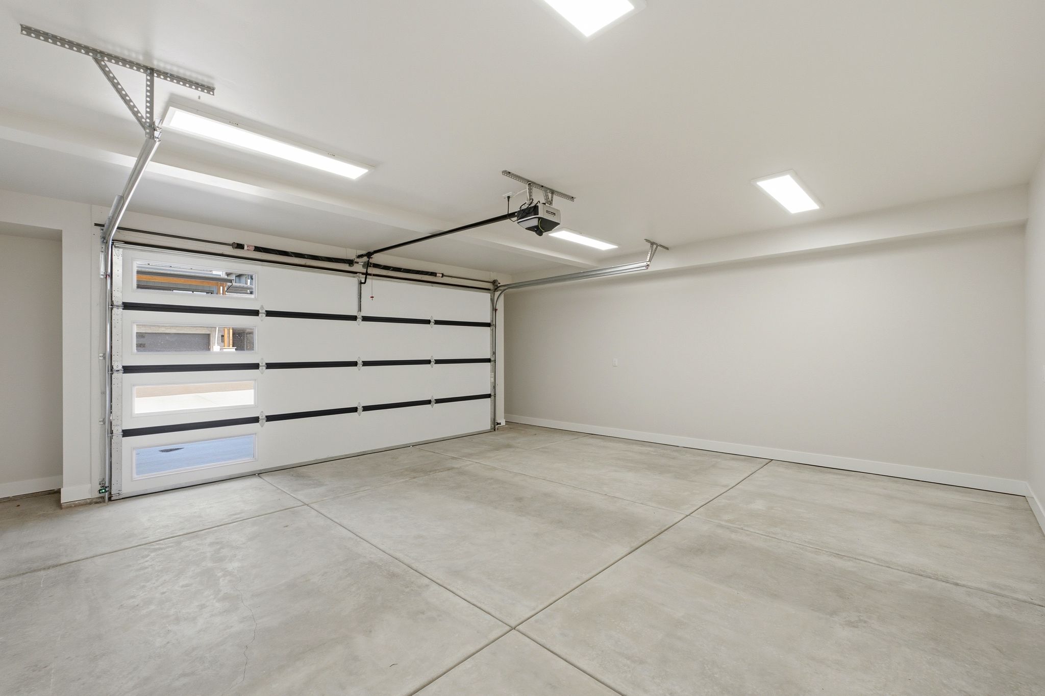 Spacious garage with a modern white sectional garage door featuring horizontal window panels, a concrete floor, and integrated ceiling lighting
