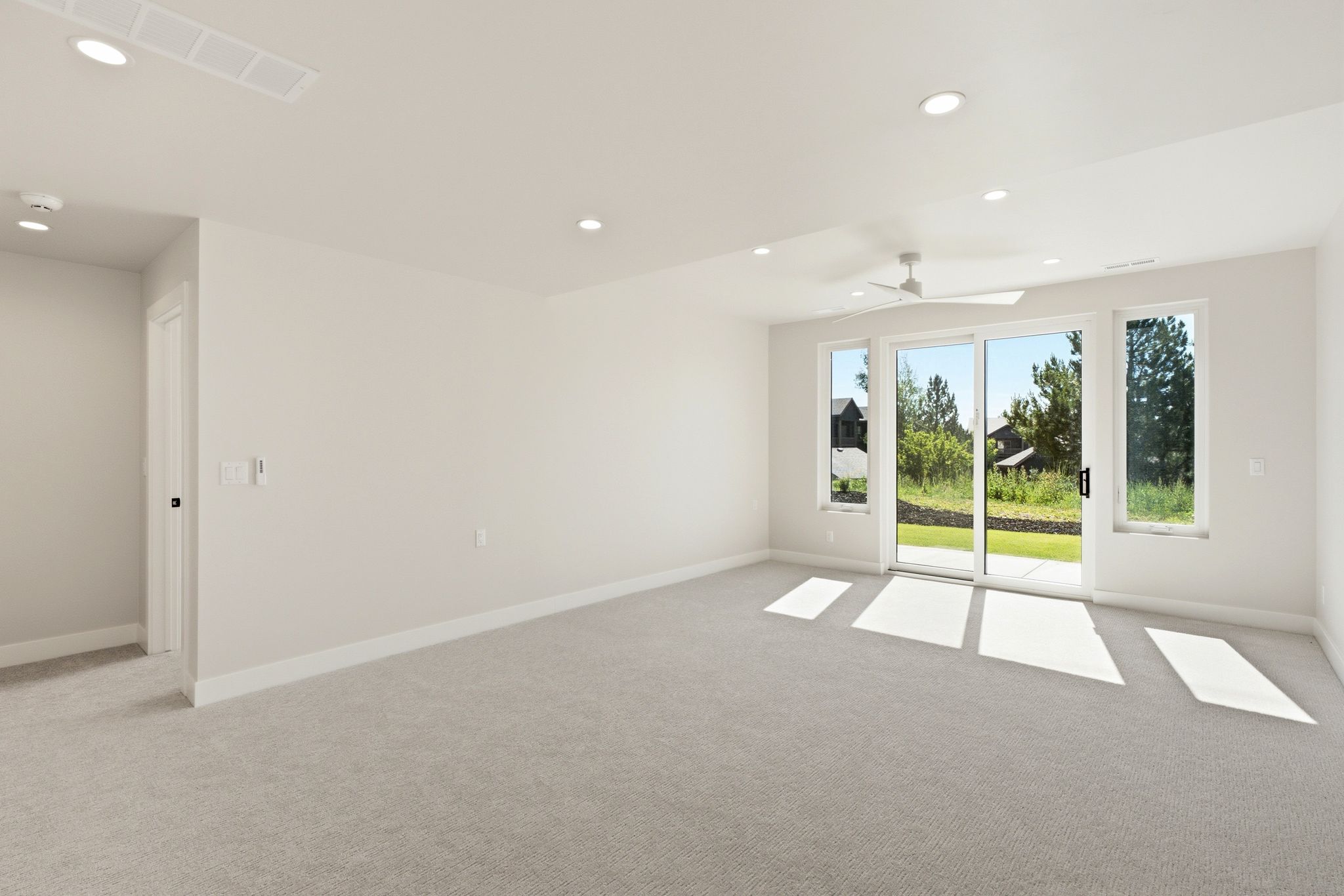 Spacious room featuring light gray carpet, white walls, recessed lighting, and a modern ceiling fan