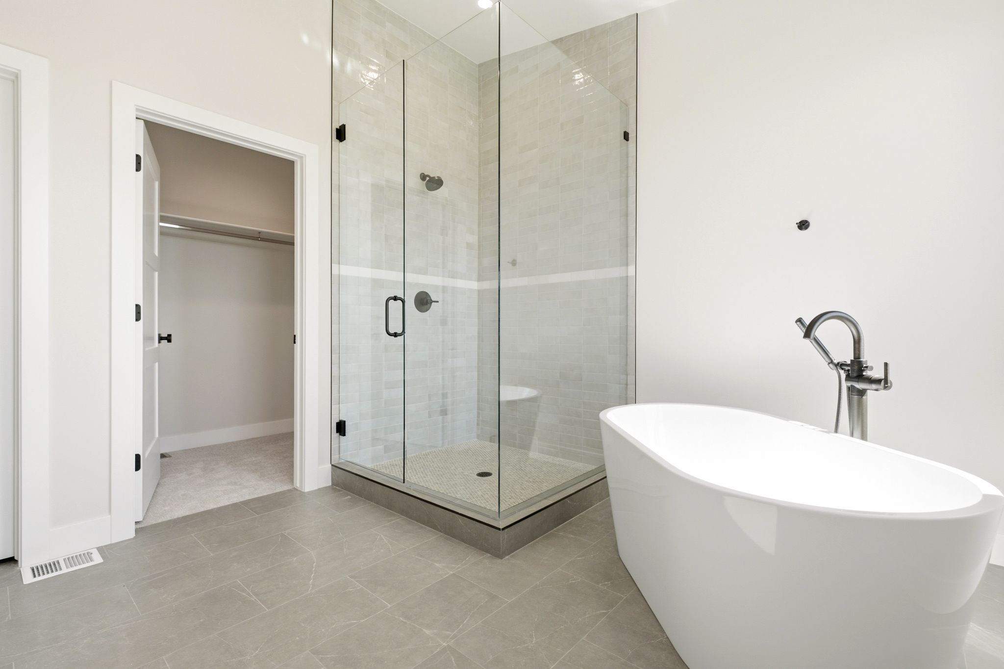 Freestanding soaking tub with chrome fixtures, glass-enclosed shower with tile surround, and large format tile flooring