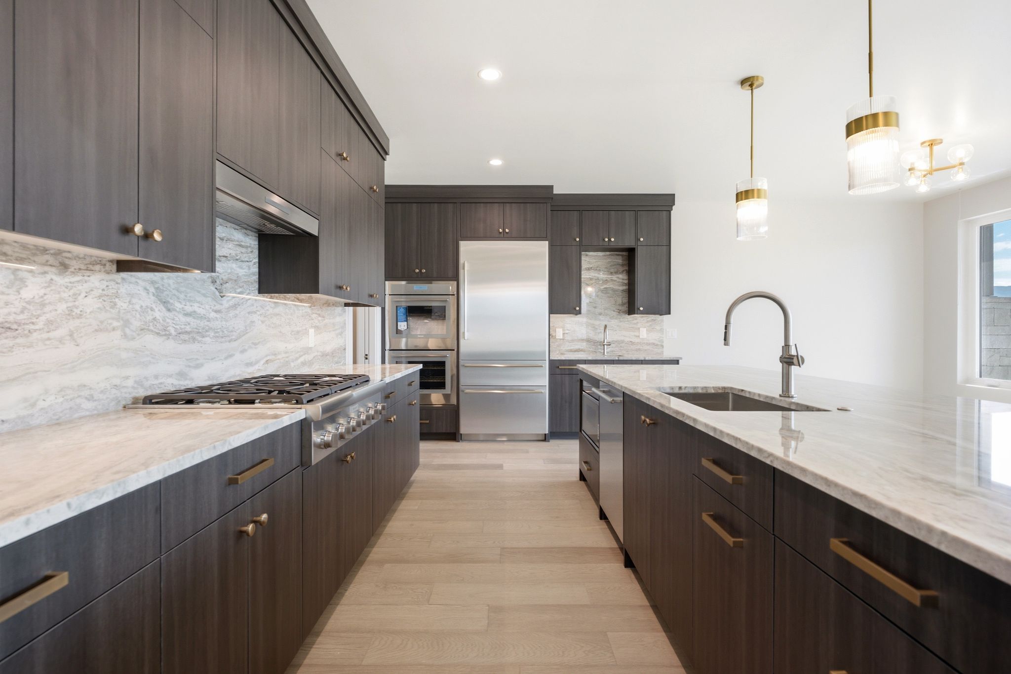 Gourmet kitchen featuring dark wood-finish cabinetry, light-toned countertops, a gas range with a stainless steel hood, a built-in oven, and a large central island with an undermount sink