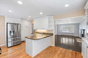 Kitchen featuring stainless steel refrigerator with ice dispenser, open shelves, a peninsula, white cabinets, and recessed lighting