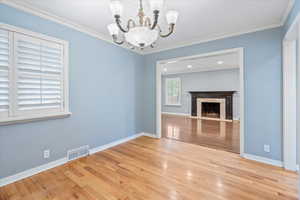 Unfurnished living room with a chandelier, wood finished floors, ornamental molding, a high end fireplace, and baseboards
