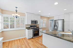 Kitchen with appliances with stainless steel finishes, a chandelier, white cabinetry, light wood-style flooring, and baseboards