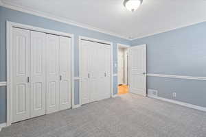Unfurnished bedroom featuring two closets, carpet flooring, ornamental molding, and baseboards