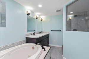 Bathroom with a jetted tub, a stall shower, double vanity, recessed lighting, and a textured ceiling