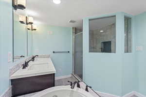 Full bath with a shower stall, double vanity, baseboards, a tub to relax in, and a textured ceiling
