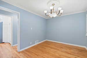 Spare room with a chandelier, light wood-style floors, baseboards, and ornamental molding