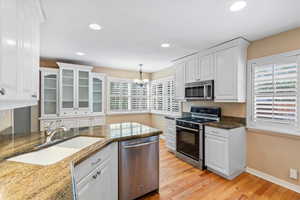 Kitchen featuring appliances with stainless steel finishes, a sink, white cabinets, a chandelier, and light wood-style floors