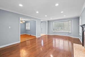 Unfurnished living room with crown molding, a fireplace with flush hearth, wood finished floors, baseboards, and a chandelier