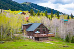 Back of property featuring a forest view, log exterior, a deck with mountain view, and a yard