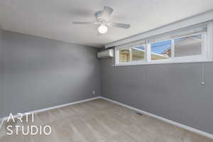 Empty room featuring a wall unit AC, light colored carpet, a ceiling fan, baseboards, and a textured ceiling