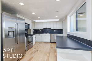 Kitchen featuring stainless steel appliances, dark countertops, white cabinetry, light wood-type flooring, and a textured ceiling