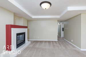 Unfurnished living room featuring carpet flooring, a raised ceiling, baseboards, and a textured ceiling