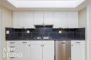 Kitchen featuring stainless steel dishwasher, a sink, dark countertops, and backsplash