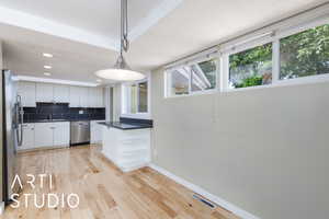 Kitchen featuring appliances with stainless steel finishes, dark countertops, white cabinetry, baseboards, and light wood finished floors