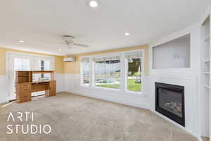 Unfurnished living room with a wall mounted air conditioner, carpet floors, ceiling fan, wainscoting, and a glass covered fireplace