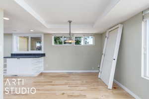 Unfurnished dining area with light wood finished floors, baseboards, recessed lighting, and a raised ceiling