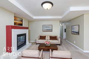 Living room featuring baseboards, a raised ceiling, a tiled fireplace, a textured ceiling, and light carpet