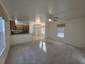 Unfurnished living room featuring a chandelier, a ceiling fan, and light colored carpet