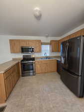 Kitchen with appliances with stainless steel finishes, a sink, brown cabinetry, and a peninsula