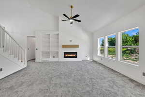 Unfurnished living room with high vaulted ceiling, ceiling fan, carpet, a glass covered fireplace, and baseboards
