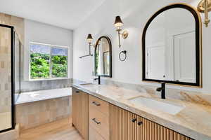 Bathroom featuring a shower stall, double vanity, a garden tub, and wood finished floors