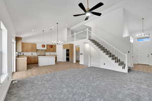 Unfurnished living room with a chandelier, high vaulted ceiling, light colored carpet, stairway, and recessed lighting