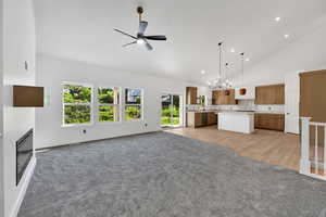 Unfurnished living room featuring light carpet, a ceiling fan, high vaulted ceiling, a chandelier, and recessed lighting