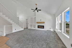 Unfurnished living room featuring high vaulted ceiling, carpet flooring, a glass covered fireplace, ceiling fan, and baseboards