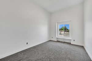 Unfurnished room featuring dark colored carpet and baseboards