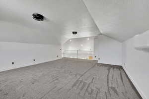 Bonus room with vaulted ceiling, a textured ceiling, carpet, baseboards, and a wall unit AC