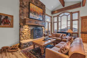 Living room with a mountain view, high vaulted ceiling, wood finished floors, a stone fireplace, and beam ceiling