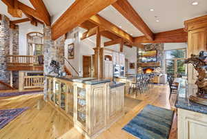 Kitchen with a large fireplace, light wood-type flooring, dark stone counters, glass insert cabinets, and lofted ceiling