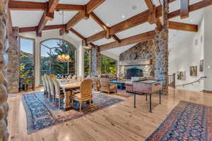 Dining space featuring high vaulted ceiling, a fireplace, beamed ceiling, light wood-type flooring, and a chandelier