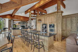 Kitchen with a breakfast bar, open floor plan, high vaulted ceiling, dark stone counters, and light brown cabinets